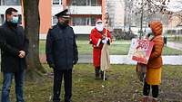 Ein Mann, ein Soldat, der Nikolaus und eine Frau stehen auf einer Grünfläche mit einem Gutschein.