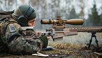 Ein Soldat liegt hinter seiner Waffe und schaut durch das Objektiv.