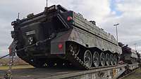 Auf einem olivfarbenen Eisenbahnwaggon steht ein olivfarbener Panzer.