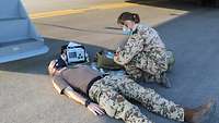 Eine Soldatin kniet während einer Übung neben einem Patienten und bereitet die medizinische Versorgung vor