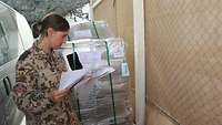 Eine Soldatin steht vor einer angelieferten Palette mit medizinischem Material