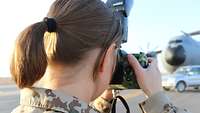 Eine Soldatin steht mit einer Kamera vor dem Flugzeug A400M und fotografiert dieses