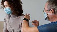 Ein Mann verspritzt eine Influenza-Impfung in den linken Oberarm einer zivilen Frau.