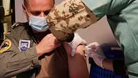 Ein General wird in seinen linken Oberarm gespritzt. Er erhält eine Impfung gegen die Grippe.