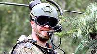 Ein Soldat mit Schutzbrille und Sprechsatz schaut aus seiner Panzerluke und zeigt den Daumen hoch.
