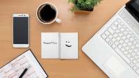 Symbolbild Stilleben Schreibtisch mit Tasse Kaffee, Laptop, Kalender und Smartphone 