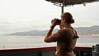 Eine Soldatin blickt mit einem Fernglas aufs Meer hinaus 