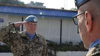Ein Soldat mit blauem Barett steht vor einem anderen und grüßt militärisch