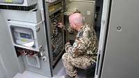 Ein Soldat kniet in einem Systemcontainer vor elektronischen Bedienelementen und überprüft diese