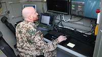 Ein Soldat sitzt in einem Systemcontainer, vor ihm vier Bildschirme und drei Tatstaturen 