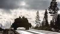 Kampfpanzer fahren über eine verschneite Straße durch einen Wald.