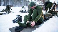 Soldaten wechseln ihre Kleidung auf Matten in einer verschneiten Landschaft.