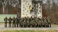 Zahlreiche Soldaten stehen und hocken als Gruppe vor einer Kletterturm aus grauem Beton.