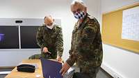 Zwei Soldaten im Feldanzug in einem Besprechungsraum betrachten den Inhalt eines blauen Aktenordners