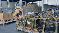 Ein Soldat spannt große, schwere Kisten und Gepäckstücke auf eine Metallpalette