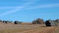 Vier Panzerhaubitzen stehen feuerbereit, aber mit großen Abständen zueinander im Gelände.