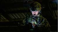 Ein Soldat mit Helm schaut in der Dunkelheit auf einen leuchtenden Digitaltransponder.