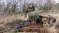 Ein Soldat liegt im hohen Gras hinter einem Gewehr.