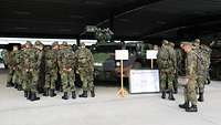 In einer großen, offenen Halle stehen zahlreiche Soldaten vor einem Militärfahrzeug.