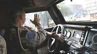 Ein Soldat fährt ein gepanzertes Fahrzeug und winkt aus dem Fenster Kindern zu, die am Straßenrand stehen