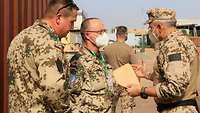 Drei Soldaten stehen sich gegenüber und reden miteinander, ein Soldat hält einen Umschlag in der Hand