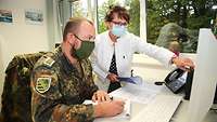 Ärztin steht neben einem Soldaten, der am Schreibtisch sitzt, und zeigt auf dem Bildschirm.
