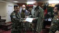 Zwei deutsche Soldaten tragen ein afghanisches Gewand, ein afghanischer Soldat überreicht eine Urkunde an diese 