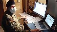 Ein Soldat sitzt in einem dunklen Zimmer vor einem Computer und einem Laptop