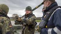 Auf der Weser: Drei Soldaten stehen auf einer Fähre, der in der Mitte erklärt etwas.