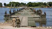 Auf einem Fluss schwimmt eine lange Schwimmbrücke aus mehreren Amphibienfahrzeugen.