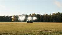 A truck being driven across a field ejecting canisters. A smoke screen emerging from the canisters