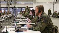 Zwei in Uniform gekleidete Soldaten sitzen an einem Einzeltisch und telefonieren über ein Headset. 