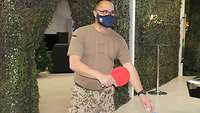 Ein Soldat mit Mund-Nasen-Schutz steht mit Schläger an einer Tischtennisplatte