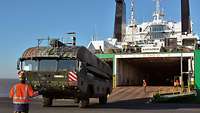 Camouflage-colored amphibious vehicle in front of a RoRo ship