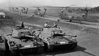 Black and white shot of tanks and helicopters in the field