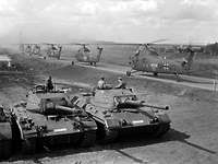 Black and white shot of tanks and helicopters in the field