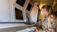 Eine Soldatin sitzt an einem Computer mit vier Bildschirmen und führt Systemtests durch