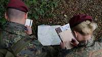 Ein Soldat und eine Soldatin hocken auf dem Boden. Sie machen sich Notizen, während sie über eine Karte gebeugt sind.