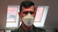 Porträtaufnahme eines Soldaten im Flecktarnanzug, der eine Mund-Nasen-Schutzmaske trägt