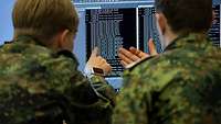 Zwei Soldaten schauen gebannt auf einen Monitor mit einem Computercode.