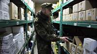 Ein Soldat steht in einem Lagerraum mit hohen Regalen, in jedem Fach stehen viele Kartons mit weiteren Materialien