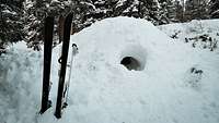 Ein Paar Ski stecken im Schnee vor einem Iglu in der weißen Schneelandschaft.