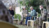 Vier Personen mit Mund-Nasen-Schutz, davon sind zwei Soldaten, sitzen in einem Garten auf Stühlen und unterhalten sich