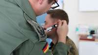 Ein Arzt untersucht einen Soldaten am Ohr.