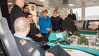 Bundeskanzlerin Angela Merke unterhält sich mit Soldaten in einem Raum mit viel Elektronik und Computern.