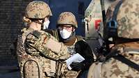Mehrere Soldatinnen und Soldaten bekleidet mit Helm, Weste und Mund-Nasen-Schutz unterhalten sich