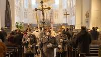 Soldaten in grauen Uniformen tragen Kreuz, Kerzen und die Heilige Schrift durch das Mittelschiff einer Domkirche.