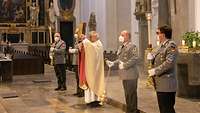 Ein Pfarrer in festlichem Ornat steht vor dem Altar, daneben Ministranten in grauer Uniform.