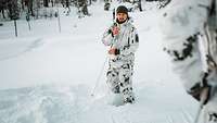 Ein Soldat in Schneetarnuniform demonstriert vor einer Ausbildungsgruppe exemplarisch die Lawinenhilfe im Schnee.