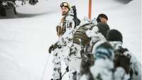 Soldaten in Schneetarnuniform stehen auf Skiern in Reihe am verschneiten Berg.